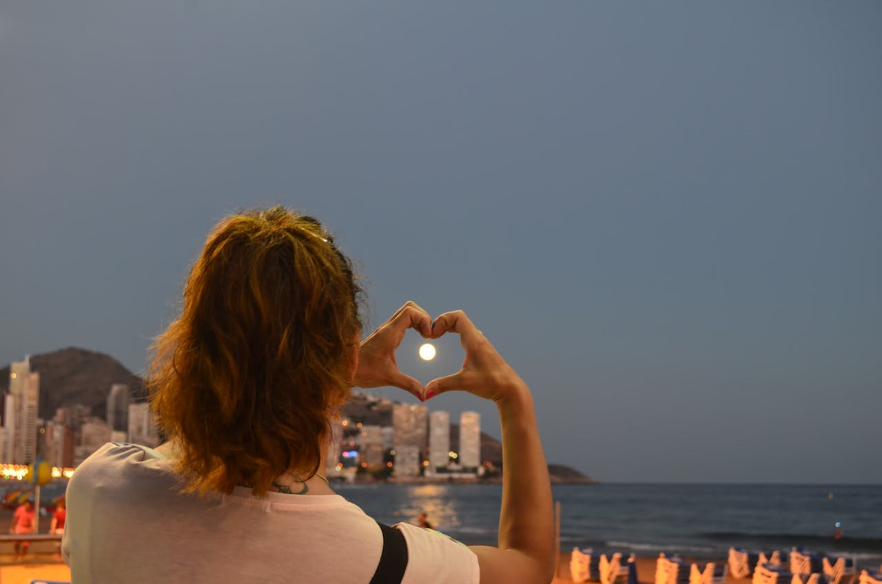 Benidorm coasline, woman making a heart shape encasing the setting sun